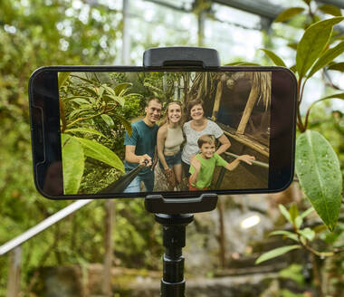 Handydisplay, das eine Familie zeigt, die gerade ein Selfie von sich in der botanika macht.