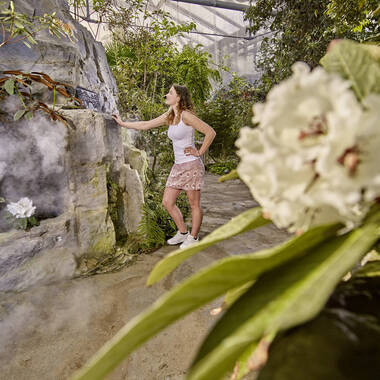 Mädchen steht an Felswand, umgeben von tropischen Pflanzen